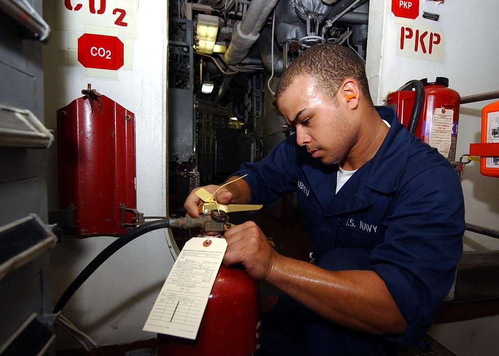A man inspects and maintains a fire extinguisher in a workshop setting.